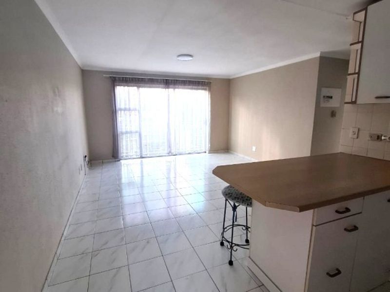 Open plan living area featuring tiled flooring and a kitchen breakfast bar, leading to a sliding glass door with access to the balcony.