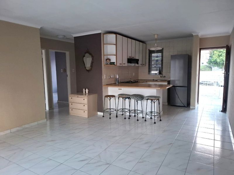 Open-plan living area featuring a functional kitchen with breakfast bar, tiled flooring, and direct access to an outdoor space.