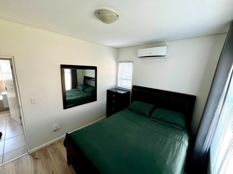 A well-maintained bedroom featuring laminate flooring, a wall-mounted split-system air conditioner, and natural light through venetian blinds.