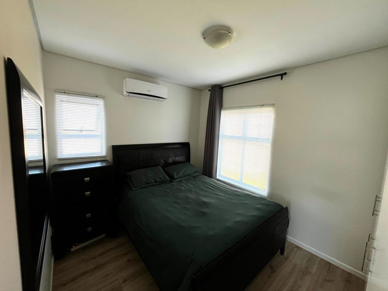 A well-maintained bedroom featuring laminate flooring, a split-system air conditioner, and dual windows with venetian blinds for natural light control.