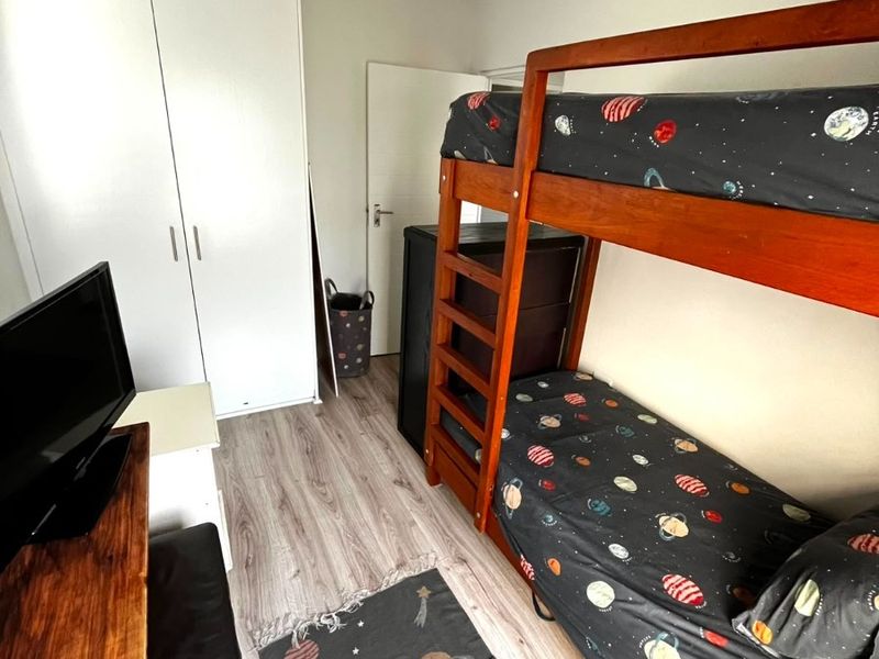 A functional bedroom featuring light-toned laminate flooring and a white built-in wardrobe, providing practical storage space.