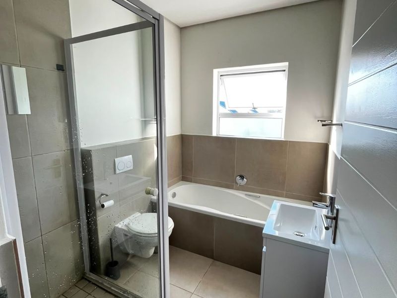 A modern, well-maintained bathroom featuring a glass shower enclosure, a built-in bathtub, a wall-hung toilet, and a vanity basin with neutral tiled finishes.