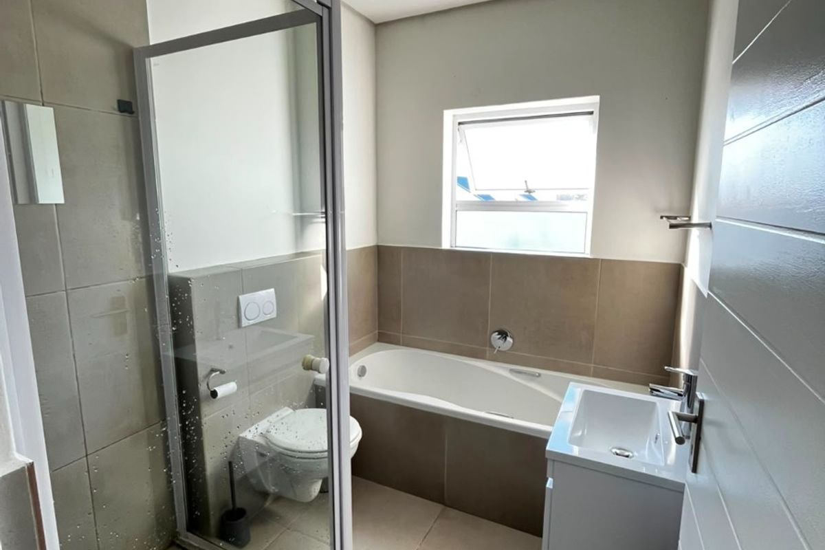 A modern, well-maintained bathroom featuring a glass shower enclosure, a built-in bathtub, a wall-hung toilet, and a vanity basin with neutral tiled finishes.