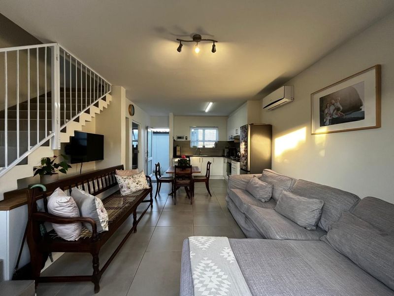 Open-plan living and kitchen area featuring tiled floors, a staircase with a metal balustrade, and a wall-mounted air conditioning unit.