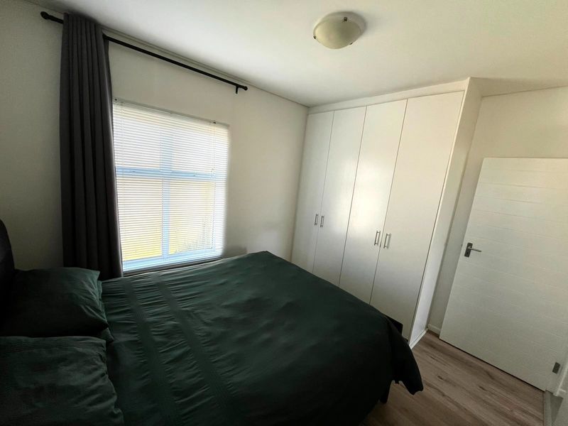 A well-maintained bedroom featuring laminate flooring, built-in cupboards, and venetian blinds, offering a clean and functional living space.