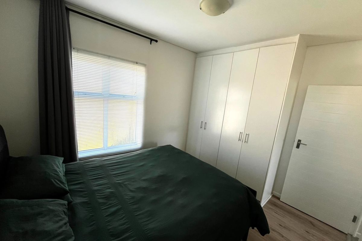 A well-maintained bedroom featuring laminate flooring, built-in cupboards, and venetian blinds, offering a clean and functional living space.
