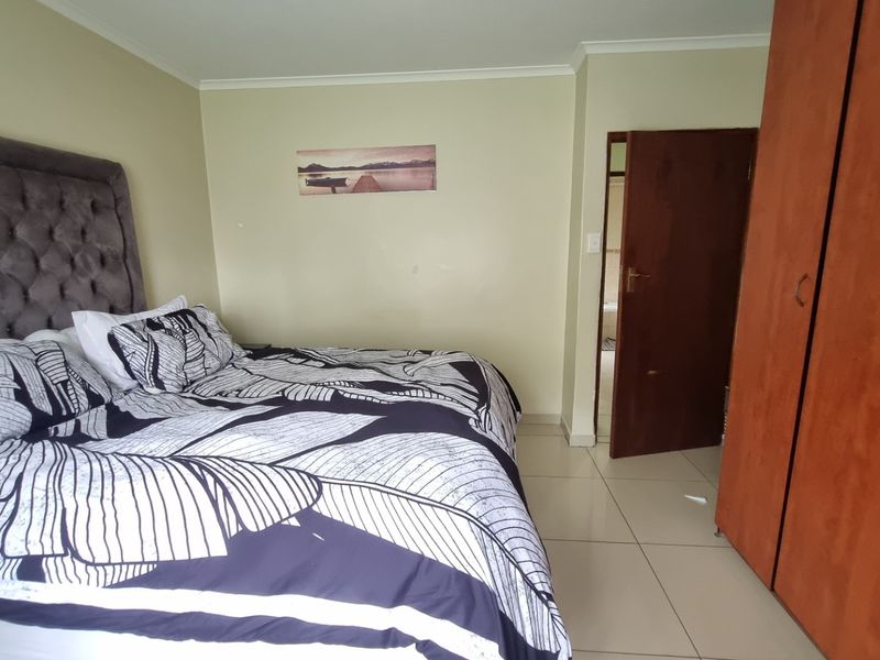 A bedroom featuring built-in wooden cupboards, tiled flooring, and neutral wall finishes, providing a functional and well-lit sleeping space.