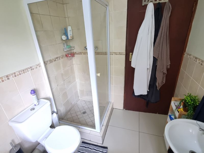 A functional bathroom featuring a corner shower enclosure, a standard toilet, and a wall-mounted basin with tiled walls and flooring.