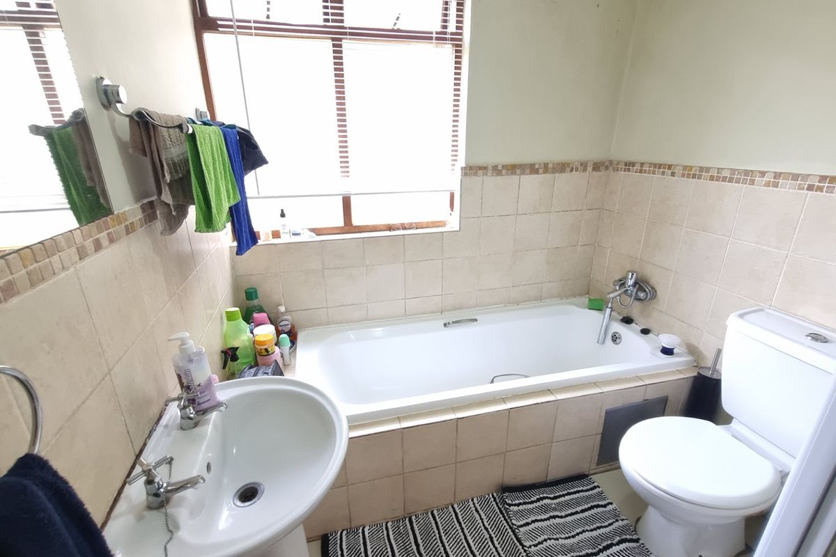A functional bathroom featuring a built-in bathtub, pedestal basin, and toilet with neutral wall tiling and a window for natural light.