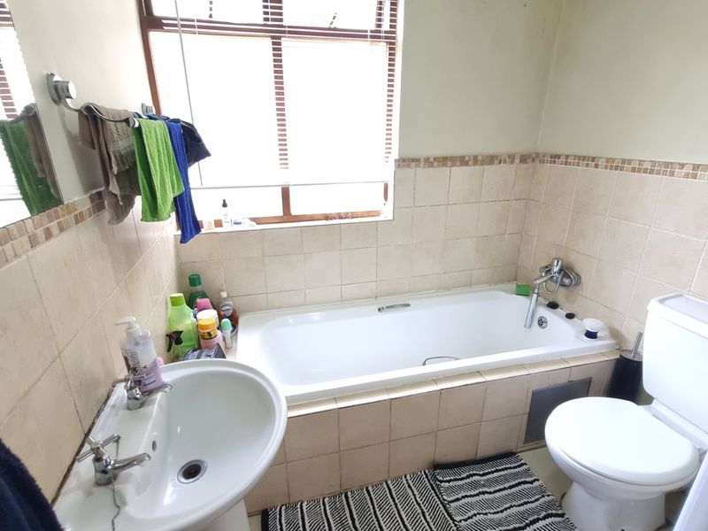 A functional bathroom featuring a built-in bathtub, pedestal basin, and toilet with neutral wall tiling and a window for natural light.