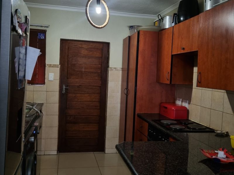 A functional kitchen featuring dark wood cabinetry, granite countertops, a built-in electric hob, and tiled flooring with direct access to an exterior door.