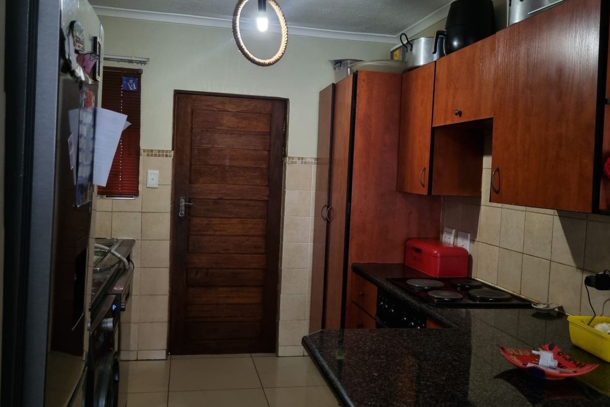 A functional kitchen featuring dark wood cabinetry, granite countertops, a built-in electric hob, and tiled flooring with direct access to an exterior door.