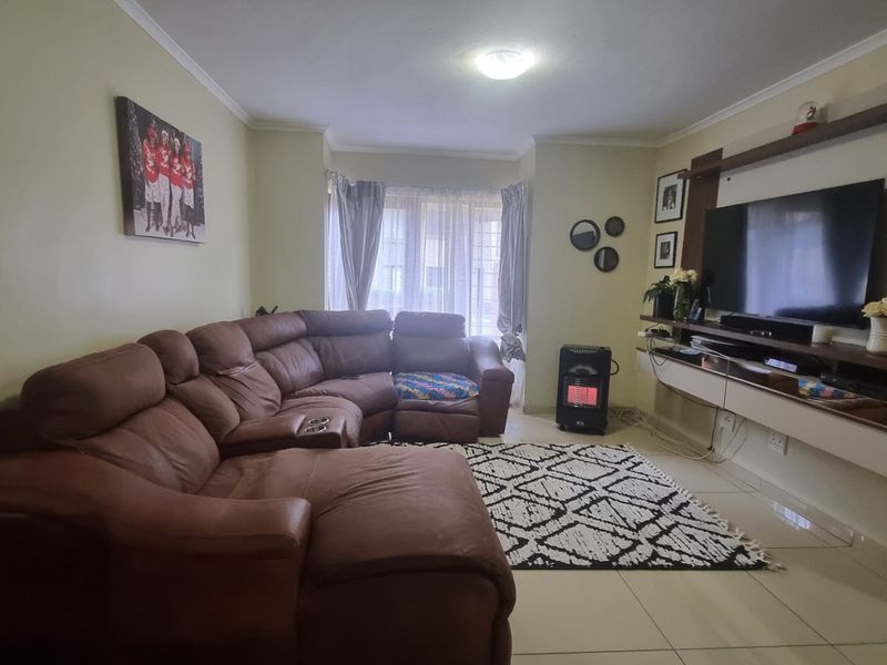 A comfortable living room featuring tiled flooring, a built-in media console, and a large bay window allowing natural light into the space.