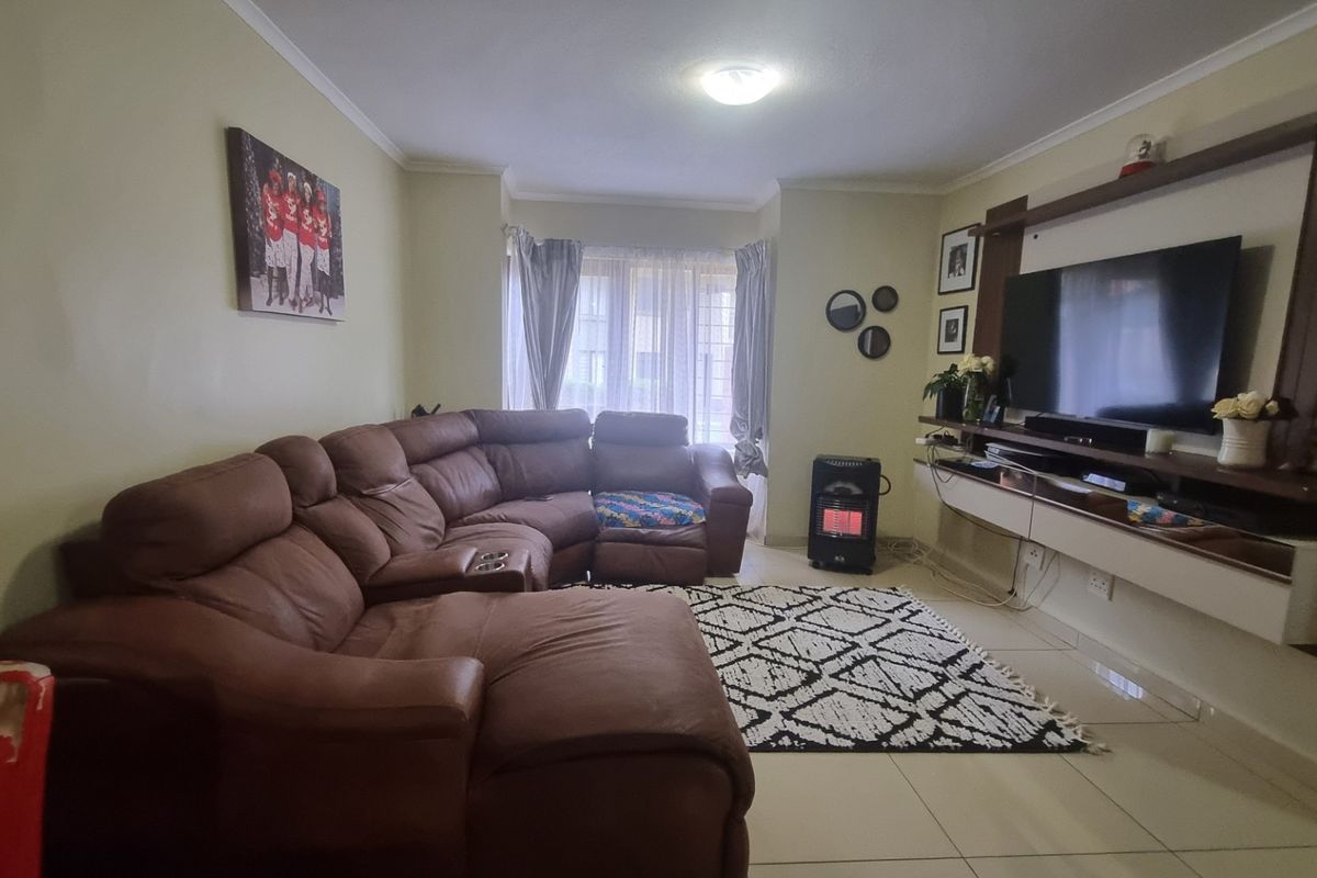 A comfortable living room featuring tiled flooring, a built-in media console, and a large bay window allowing natural light into the space.