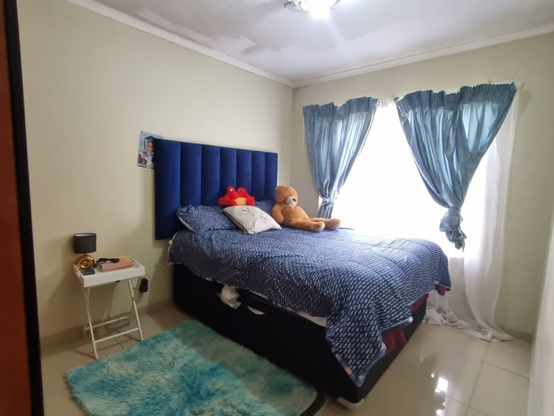A standard bedroom featuring tiled flooring and a large window with curtains, providing natural light to the space.