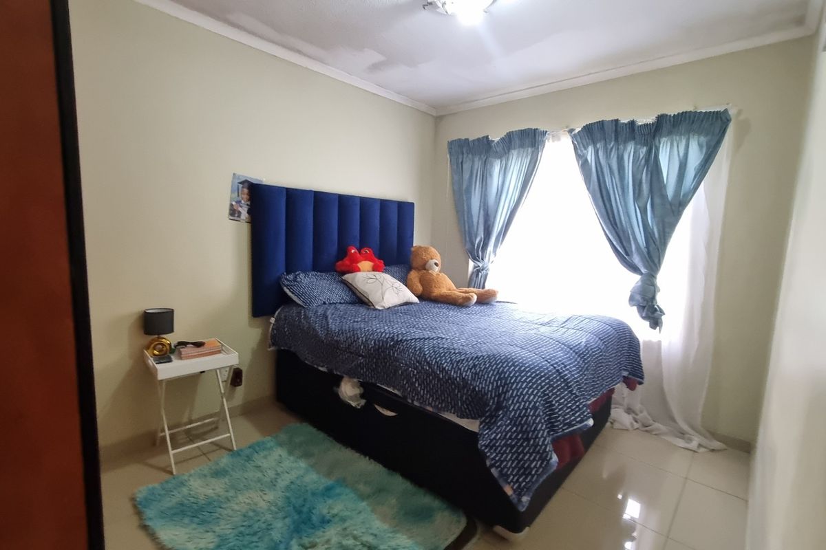 A standard bedroom featuring tiled flooring and a large window with curtains, providing natural light to the space.