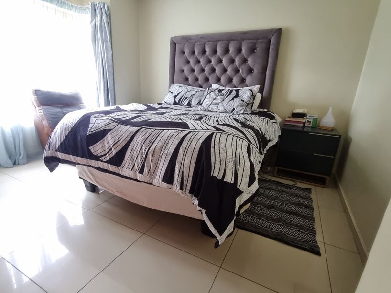 A well-lit bedroom featuring neutral tiled flooring and large windows, providing a comfortable and functional living space.