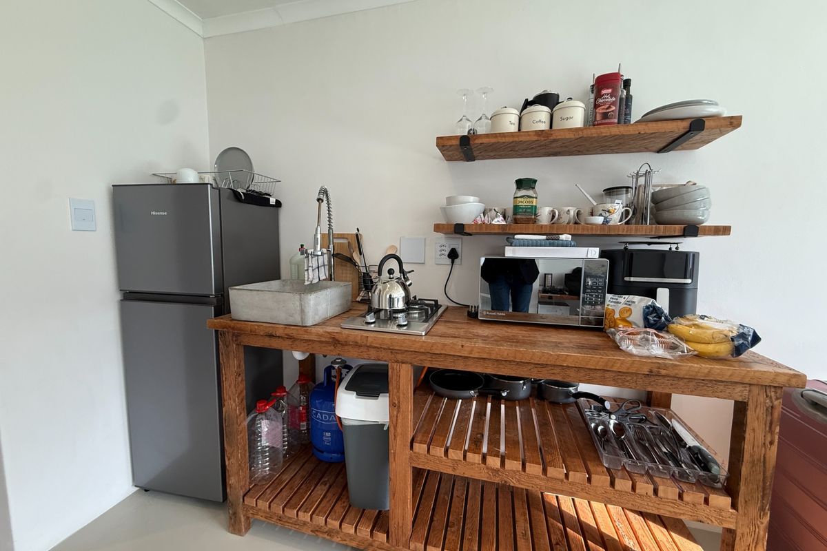 Compact kitchenette featuring a wooden workbench, integrated sink, gas hob, and open shelving for storage.