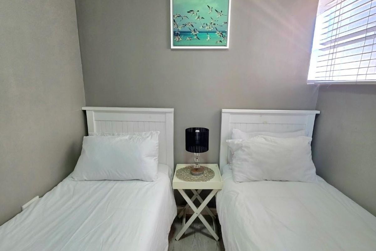 A compact bedroom featuring light-toned flooring, neutral wall finishes, and a window fitted with horizontal blinds.
