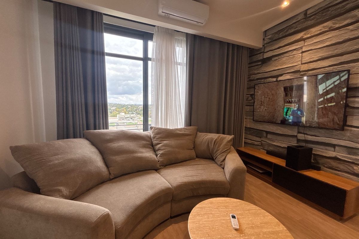 A modern living room featuring a textured stone feature wall, wood-look flooring, and a wall-mounted air conditioning unit with large windows offering exterior views.