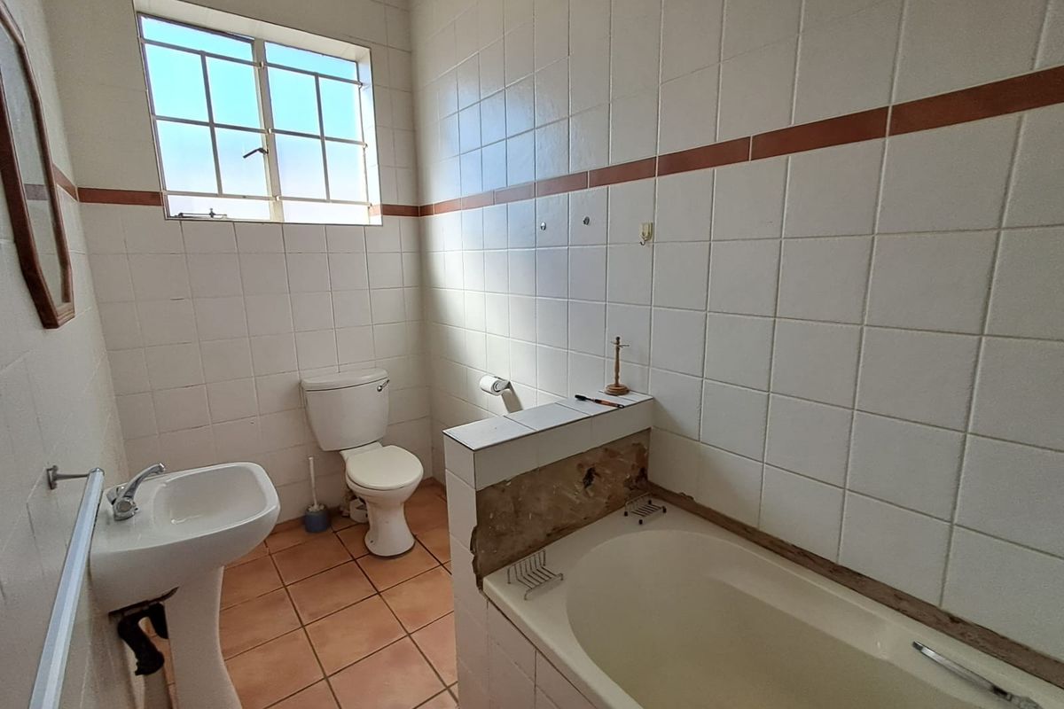 A dated bathroom featuring a pedestal basin, toilet, and a bathtub with a partially damaged tiled surround, requiring cosmetic updates.