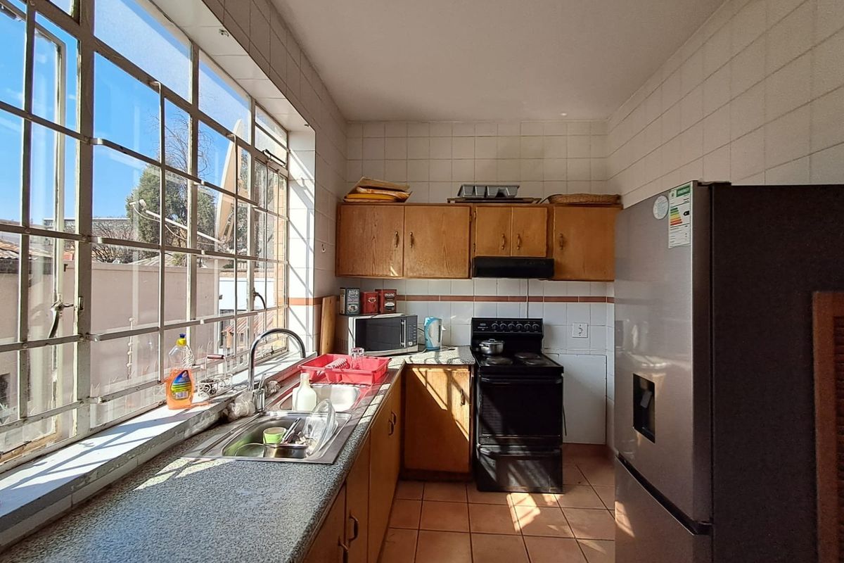 A compact kitchen featuring dated wooden cabinetry, tiled walls, a stainless steel sink, and a large window providing natural light.