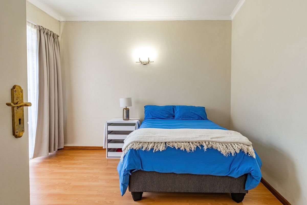A bedroom featuring laminate flooring, a wall-mounted light fixture, and a door with a brass handle, providing a functional and neutral living space.