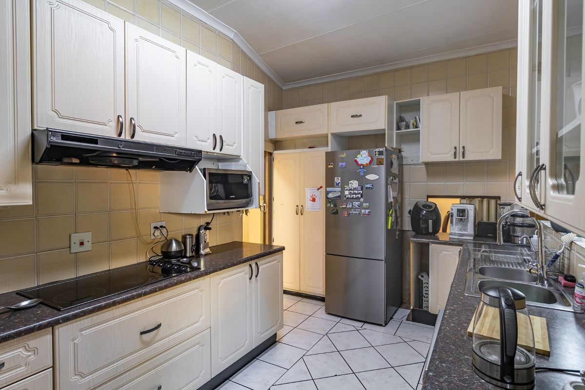 A functional kitchen featuring white cabinetry, dark laminate countertops, a built-in extractor fan, and tiled flooring.