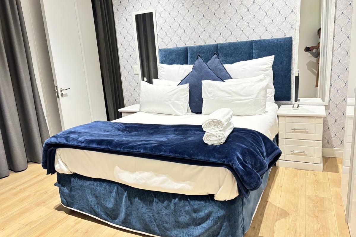 A well-maintained bedroom featuring light wood-look flooring, patterned wallpaper, and a built-in headboard design.