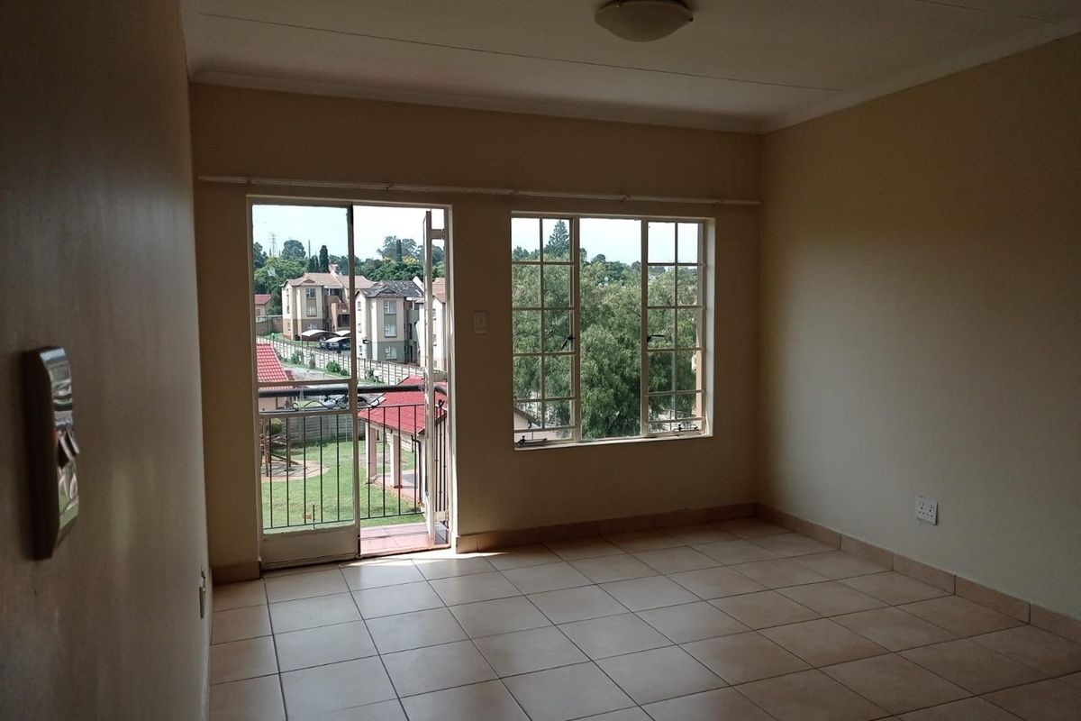 An empty living room featuring tiled flooring, large windows, and a sliding door providing access to a balcony with neighborhood views.