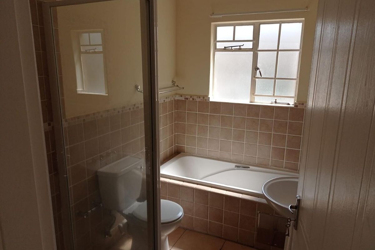 A functional bathroom featuring a built-in bathtub, separate shower enclosure, pedestal basin, and toilet with neutral tiled finishes.