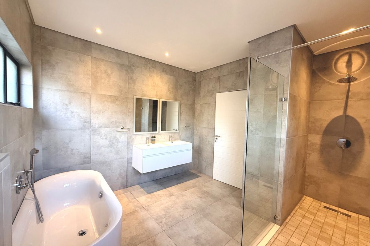 Modern, spacious bathroom featuring a freestanding bathtub, walk-in shower with glass screen, and a sleek wall-mounted double vanity with contemporary grey tiling.