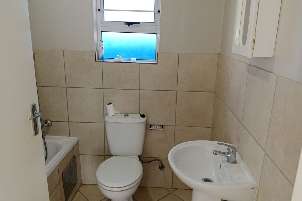 A functional bathroom featuring a pedestal basin, toilet, and bathtub with neutral wall and floor tiling.