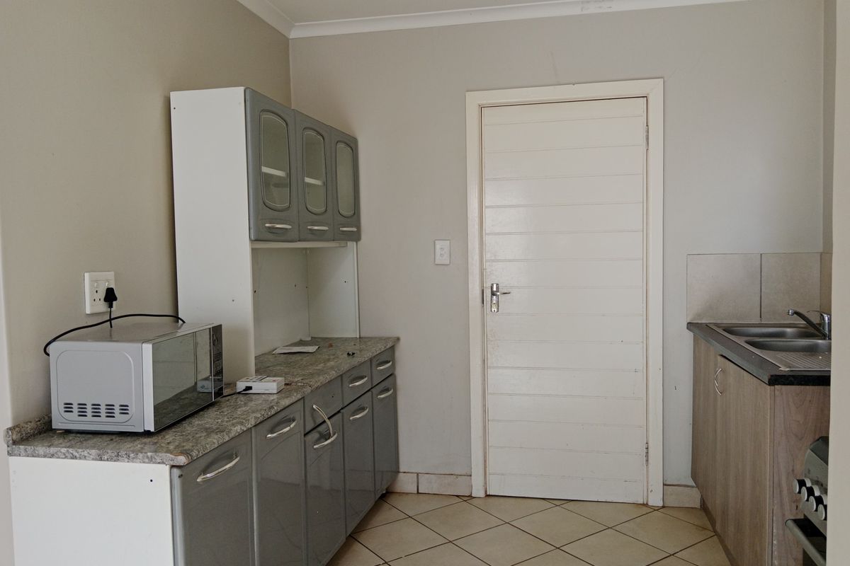 A functional kitchen area featuring grey cabinetry, granite-look countertops, a double sink, and tiled flooring.