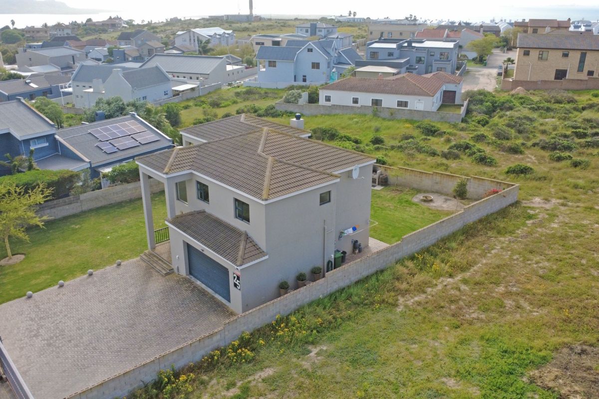 Aerial view of a two-story residential property featuring a paved driveway, garage, tiled roof, and enclosed garden area within a coastal neighborhood.
