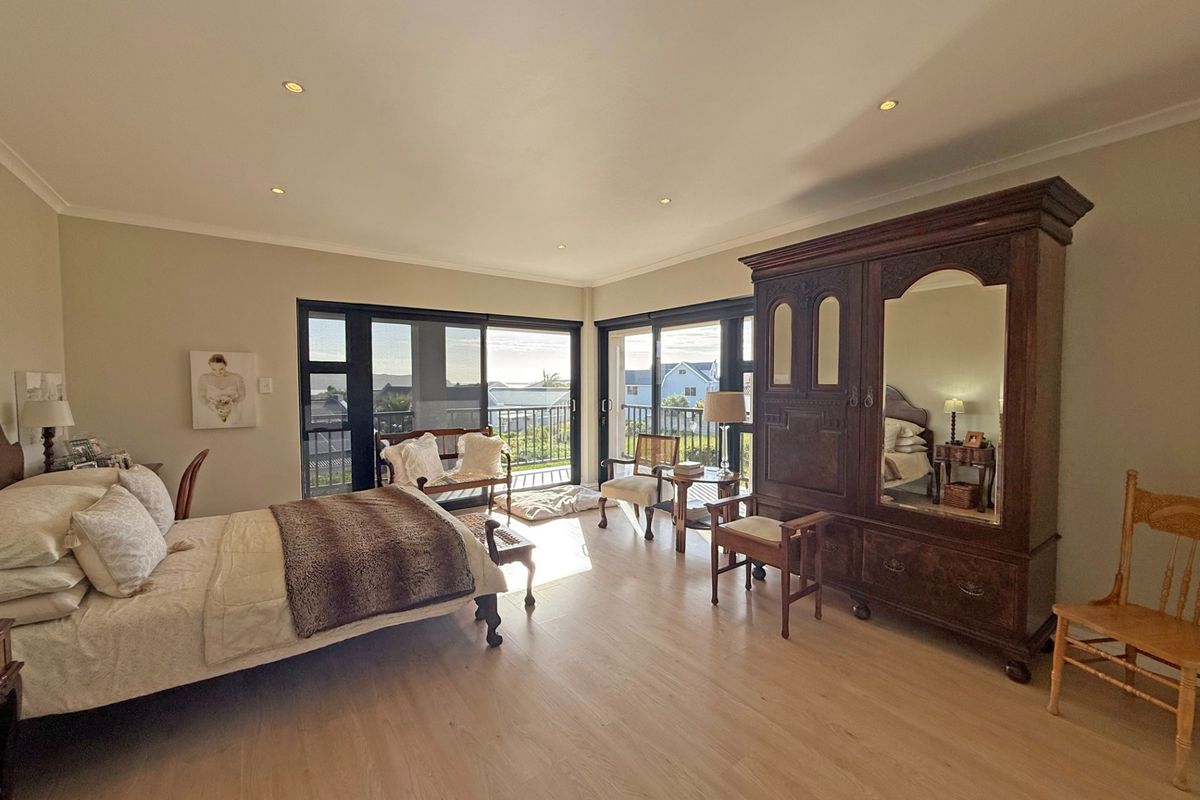 Spacious bedroom featuring light wood-look flooring, recessed ceiling lighting, and large sliding glass doors opening onto a private balcony with exterior views.