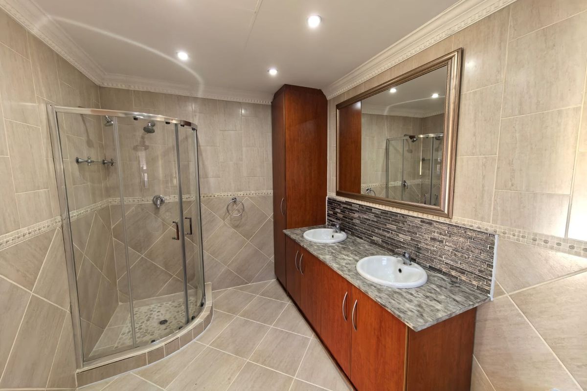 A well-maintained bathroom featuring a curved glass shower enclosure, double vanity with stone-look countertop, and full-height wall tiling.