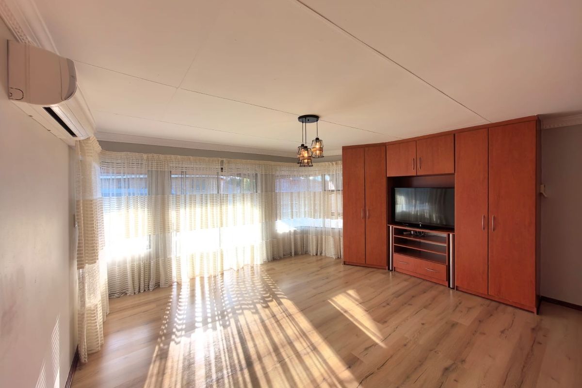 Spacious living room featuring light wood-look flooring, built-in wooden cabinetry, and a wall-mounted air conditioning unit with large windows providing natural light.