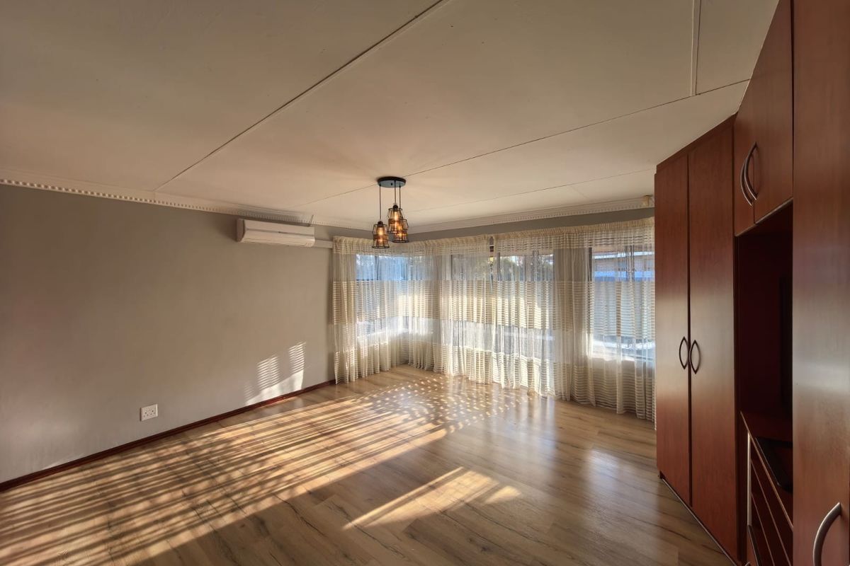 A bright and spacious bedroom featuring wood-look flooring, built-in wooden cabinetry, and a wall-mounted air conditioning unit.