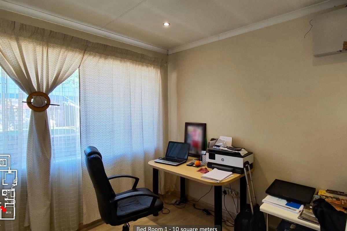 A functional bedroom featuring laminate flooring, recessed ceiling lighting, and a large window with curtaining, currently utilized as a home office space.