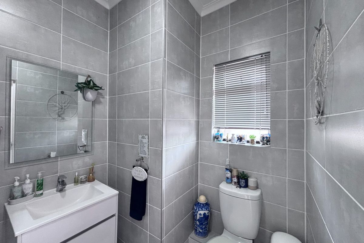 A modern bathroom featuring floor-to-ceiling grey tiling, a wall-mounted vanity with integrated basin, and a standard toilet.
