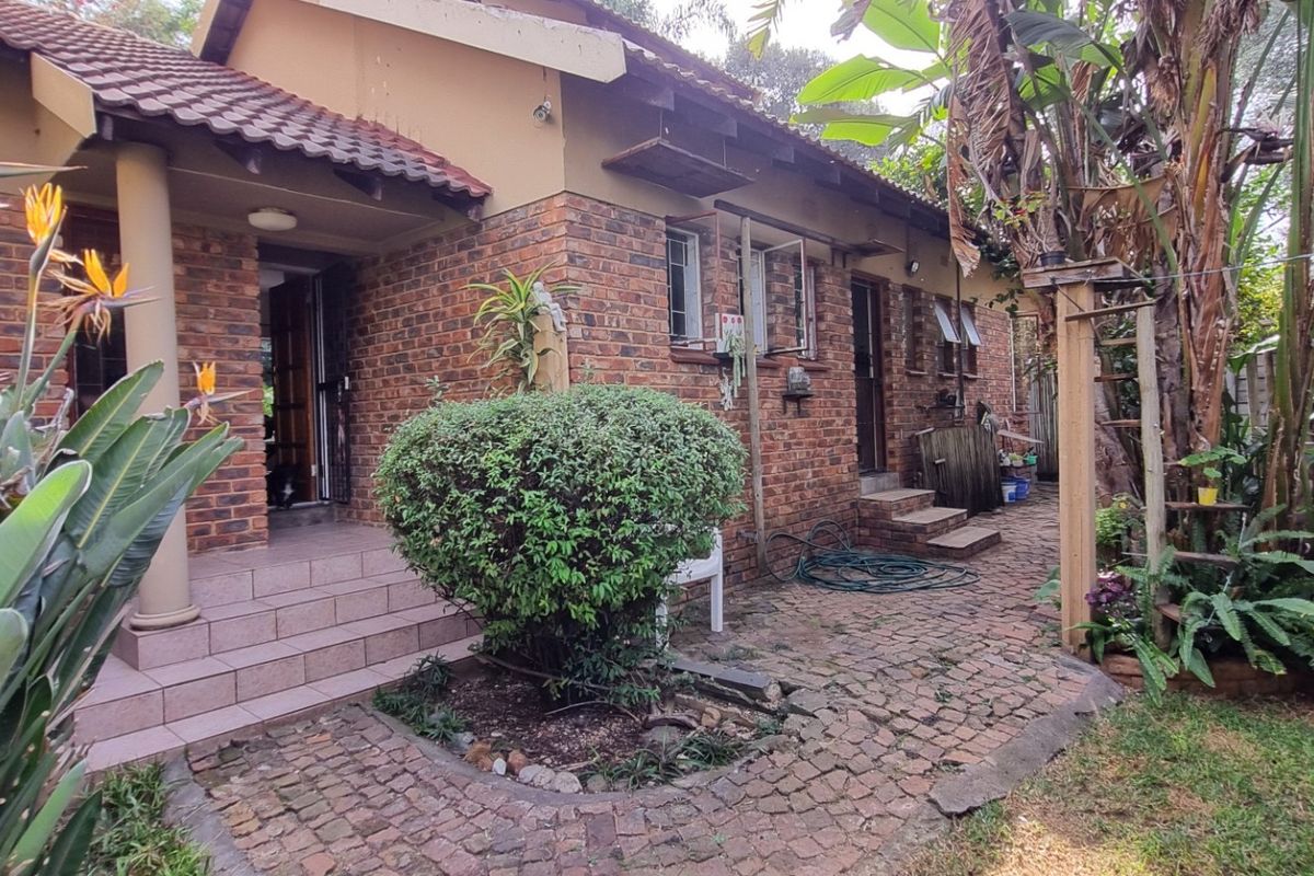 Rear view of a face-brick house featuring a tiled roof, paved patio area, and established garden surroundings.