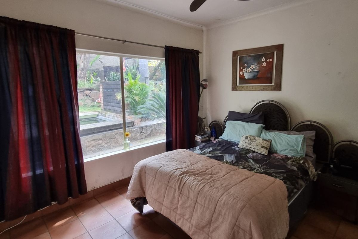 A bedroom featuring large windows with garden views, tiled flooring, and a ceiling fan.