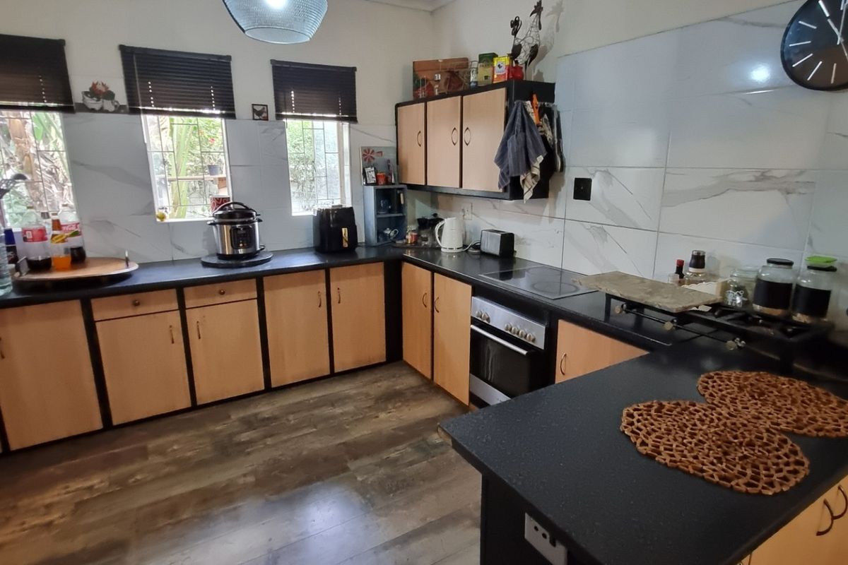 Functional kitchen featuring L-shaped layout, dark laminate countertops, built-in oven and hob, and marble-look wall tiling.