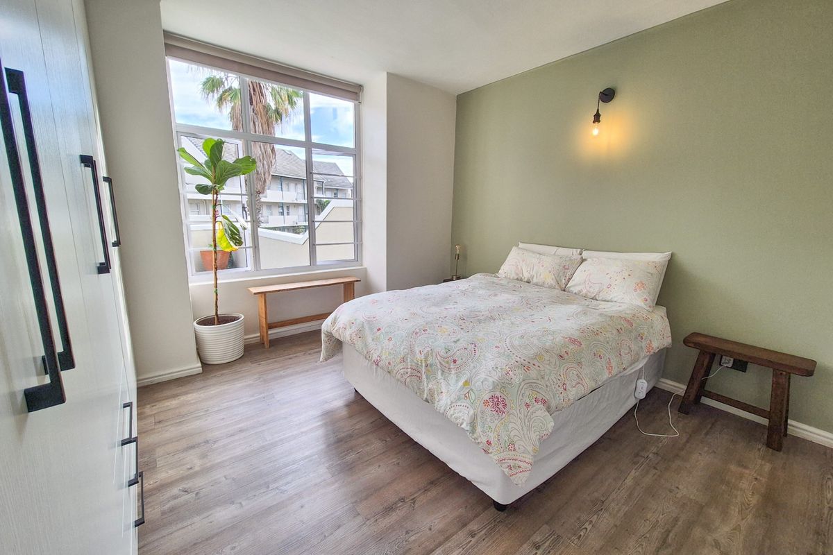 A bright and well-maintained bedroom featuring laminate flooring, a built-in wardrobe, and a large window providing natural light.