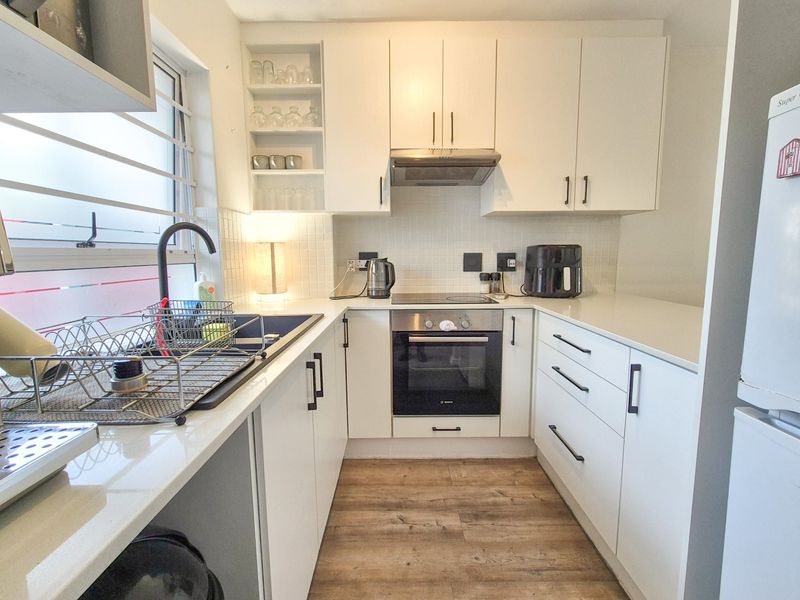 A modern, compact kitchen featuring white cabinetry, quartz countertops, integrated oven and hob, and durable laminate flooring.