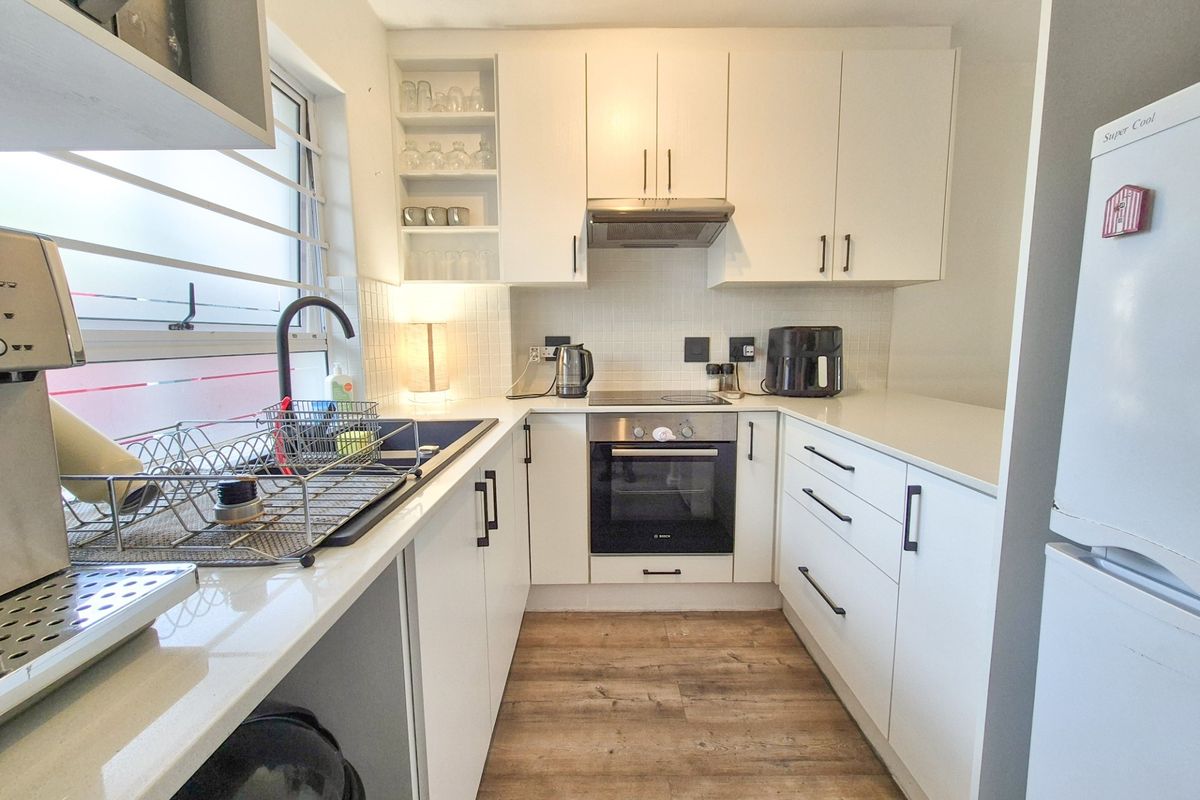 A modern, compact kitchen featuring white cabinetry, quartz countertops, integrated oven and hob, and durable laminate flooring.