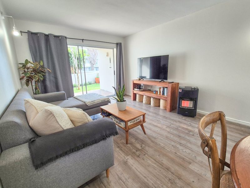 A bright living room featuring modern laminate flooring and a large sliding glass door providing direct access to the outdoor patio area.
