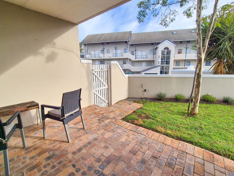 A private ground floor patio featuring brick paving, a small garden area, and a secure pedestrian gate leading to the complex grounds.