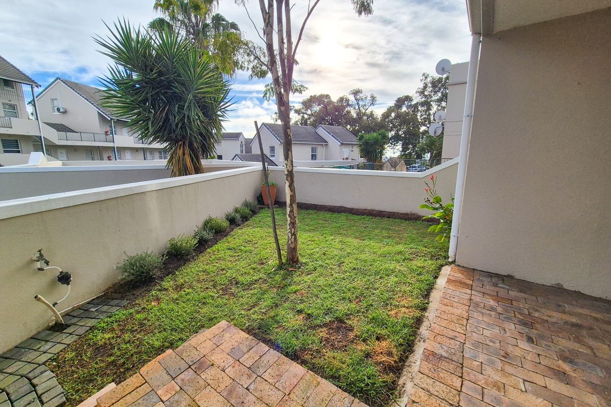 A private rear garden area featuring a paved patio, boundary walls, and a small lawn space with an external water tap.